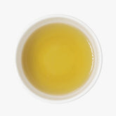 Top view of a white ceramic cup filled with Assam Green tea on a plain white background.